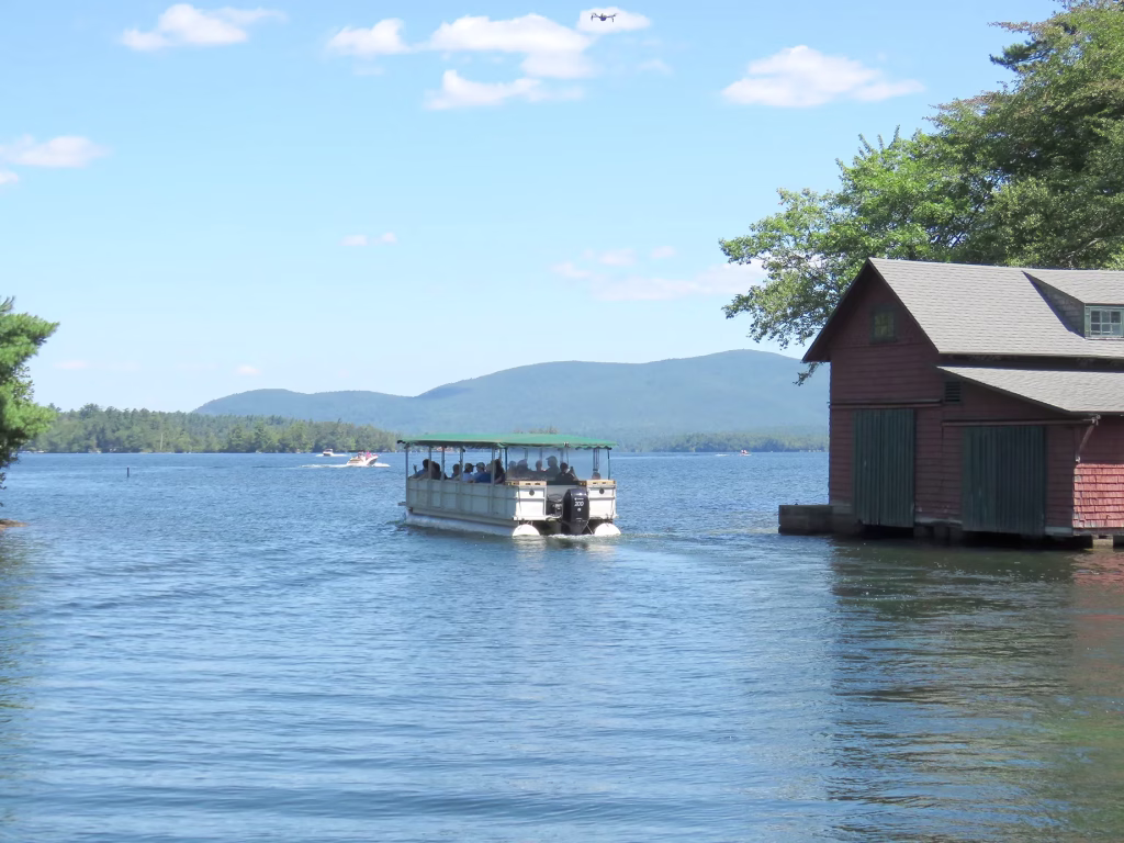 Pontoon Boat in Squam Canal by a boat house and Squam range in the background
