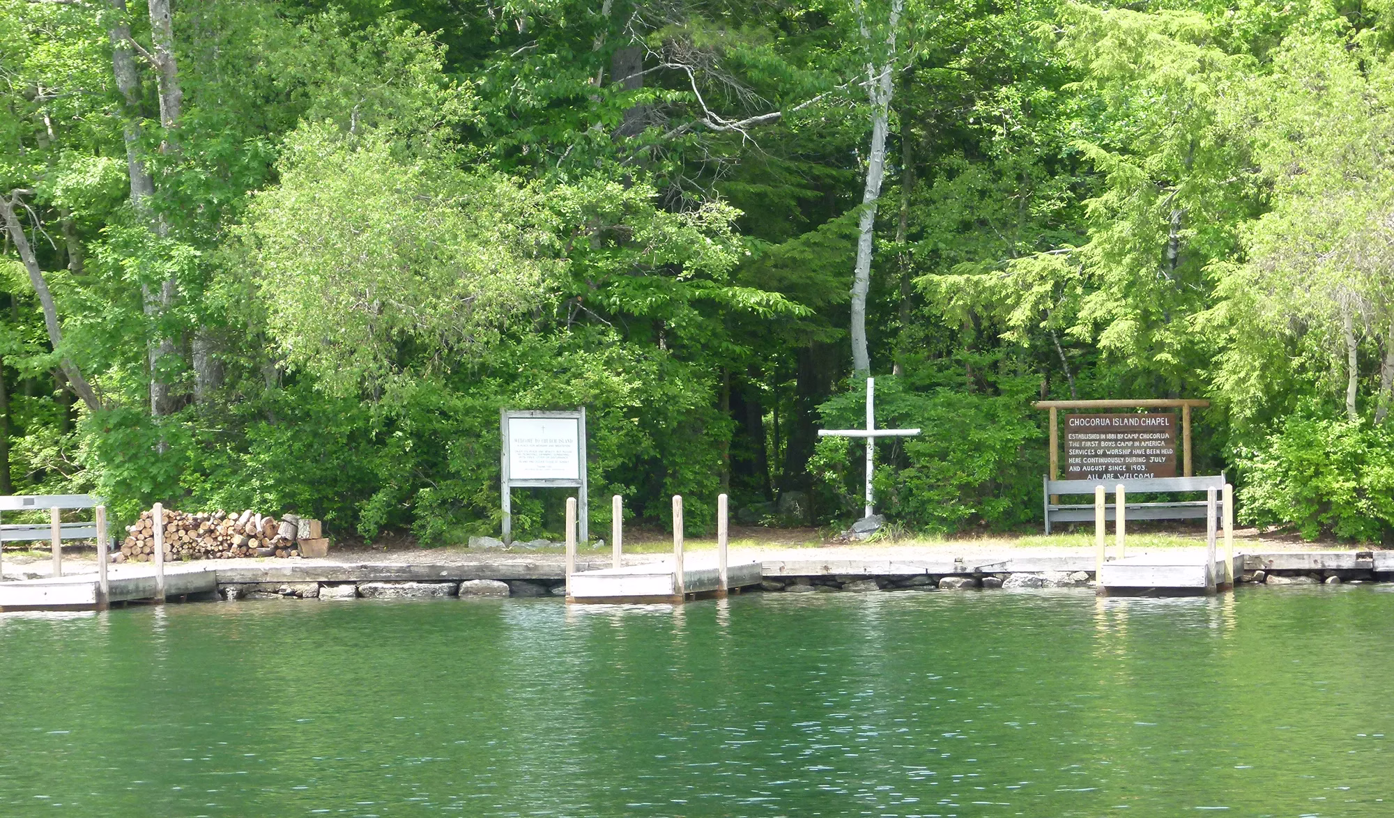 lake and forest with a wooden cross behind docks.